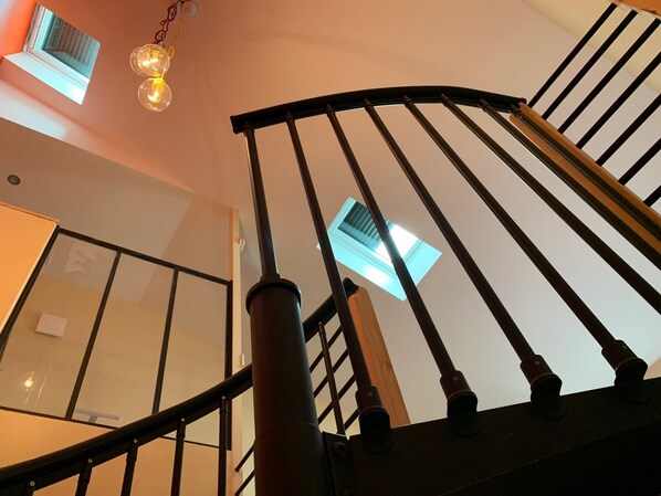 A staircase with a curved handrail and black balusters, leading to a landing with a window and a light fixture.