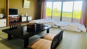 A hotel room with a bed, a desk with a computer, a chair, a table with a teapot, and a window with a view of greenery. - Hotel Tetora Resort Shizuoka Yaizu (Yaizu)