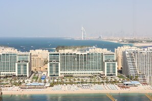 A coastal hotel with multiple high-rise buildings, a beach area with sun loungers and umbrellas, and a prominent sail-shaped building in the background.