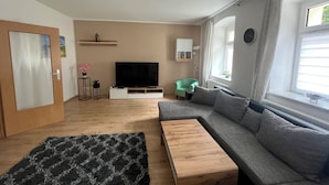 A modern living room with a sofa, a coffee table, a TV, and a window with curtains.