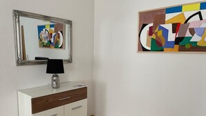 A room with a white cabinet, a mirror, and a modern abstract painting on the wall.