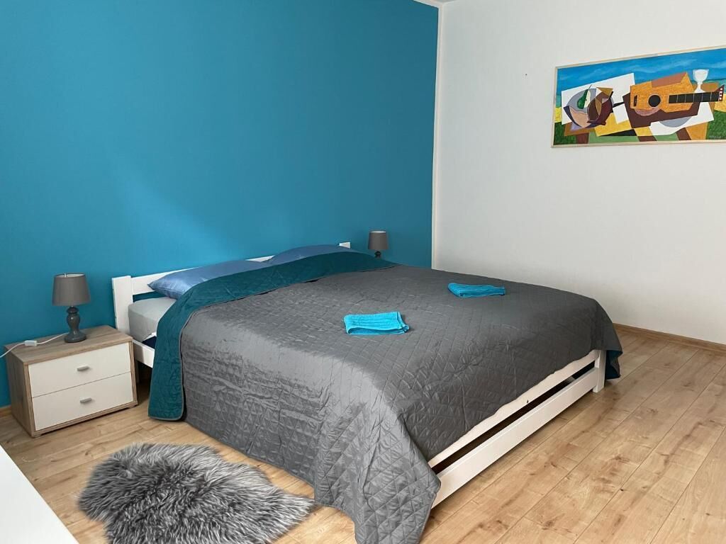 A bedroom with a bed, a nightstand, a lamp, a rug, and a painting on the wall.