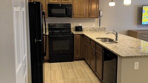 Una cocina moderna con armarios de madera, un refrigerador negro, un microondas, una estufa y un lavavajillas.