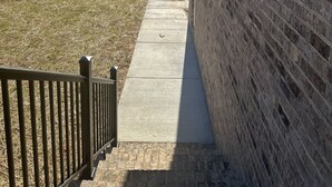 A brick building with a concrete pathway leading to a grassy area with trees and a pond. - 2BR The Bandit Suite (Lexington)