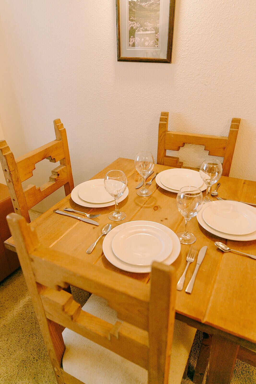 A wooden dining table set with white plates, cutlery, and wine glasses.