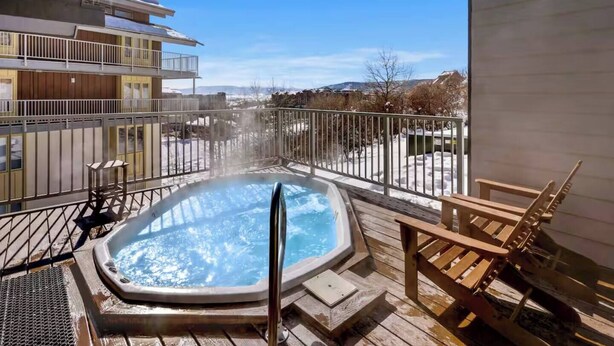 A hot tub on a wooden deck with a view of a snowy landscape and buildings in the background. - Budget Ski-In/Out+Walk to Dining (Steamboat Springs)