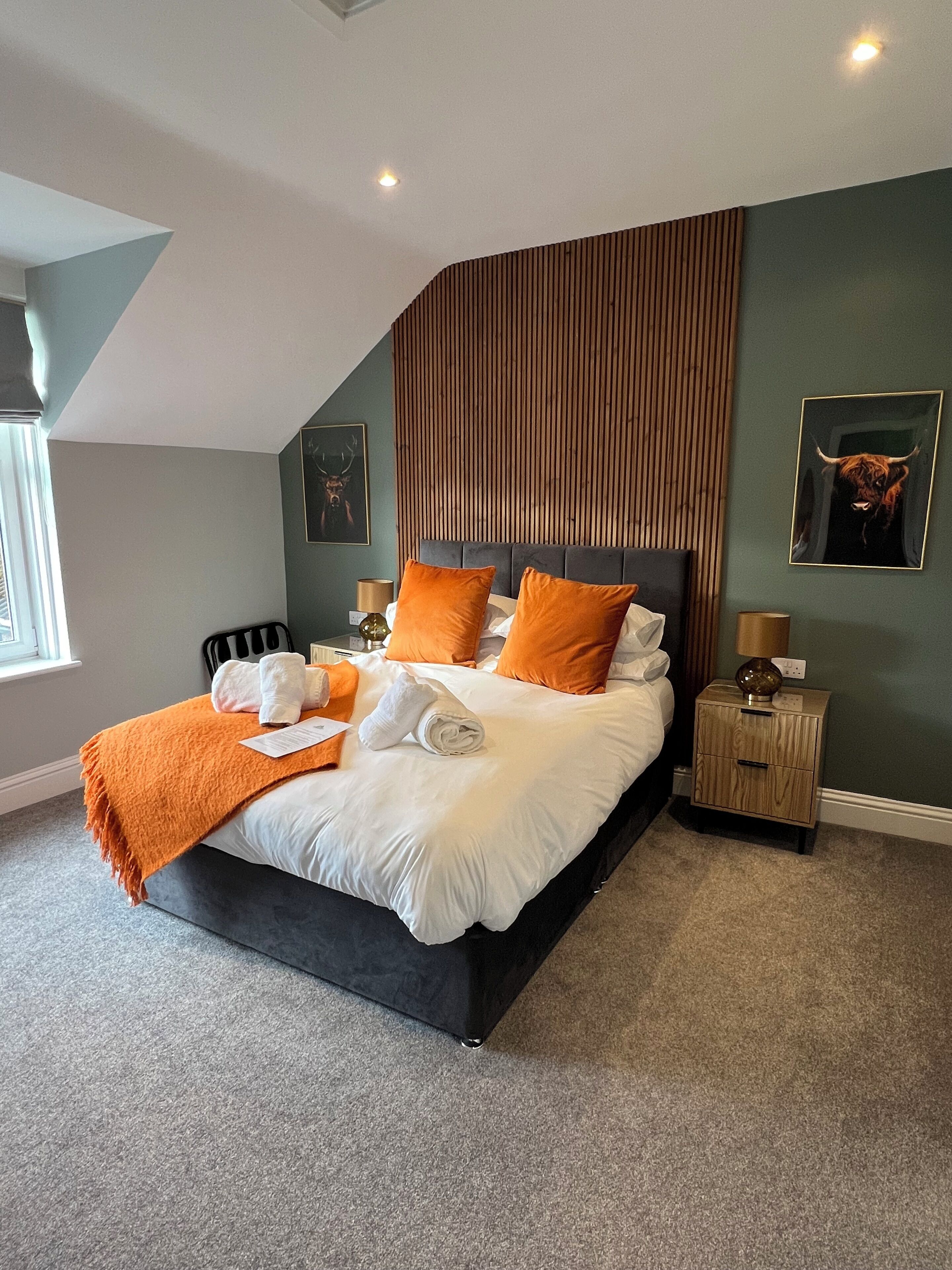 Ein Schlafzimmer mit Bett, Kissen, einem Nachttisch, einer Lampe und Bildern an den Wänden.
