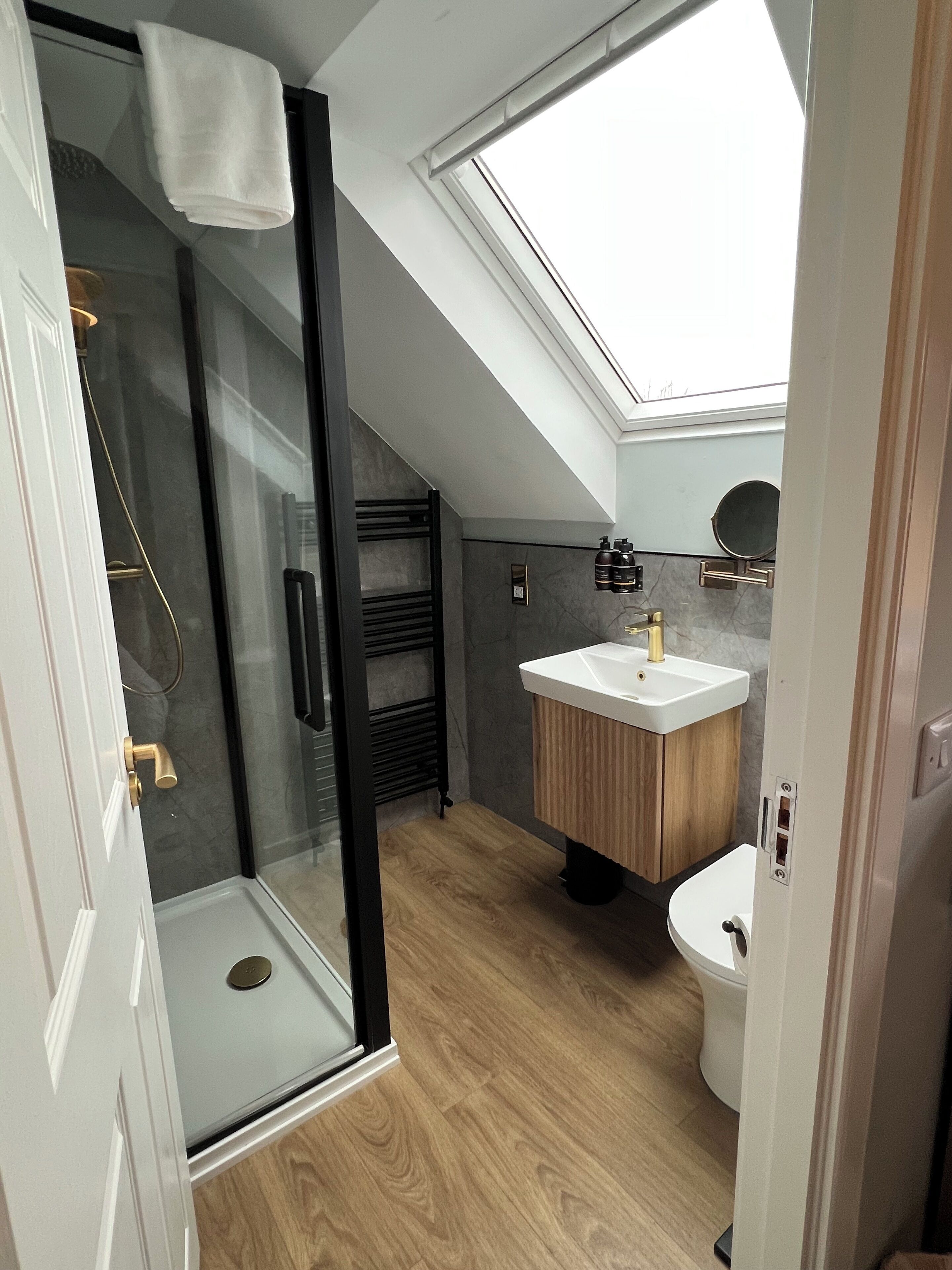 Un baño moderno con cabina de ducha de vidrio, tragaluz, tocador de madera y retrete.