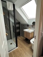 Un baño moderno con cabina de ducha de vidrio, tragaluz, tocador de madera y retrete.