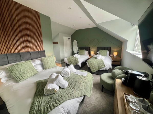 A hotel room with two beds, a TV, a kettle, and a dining area.
