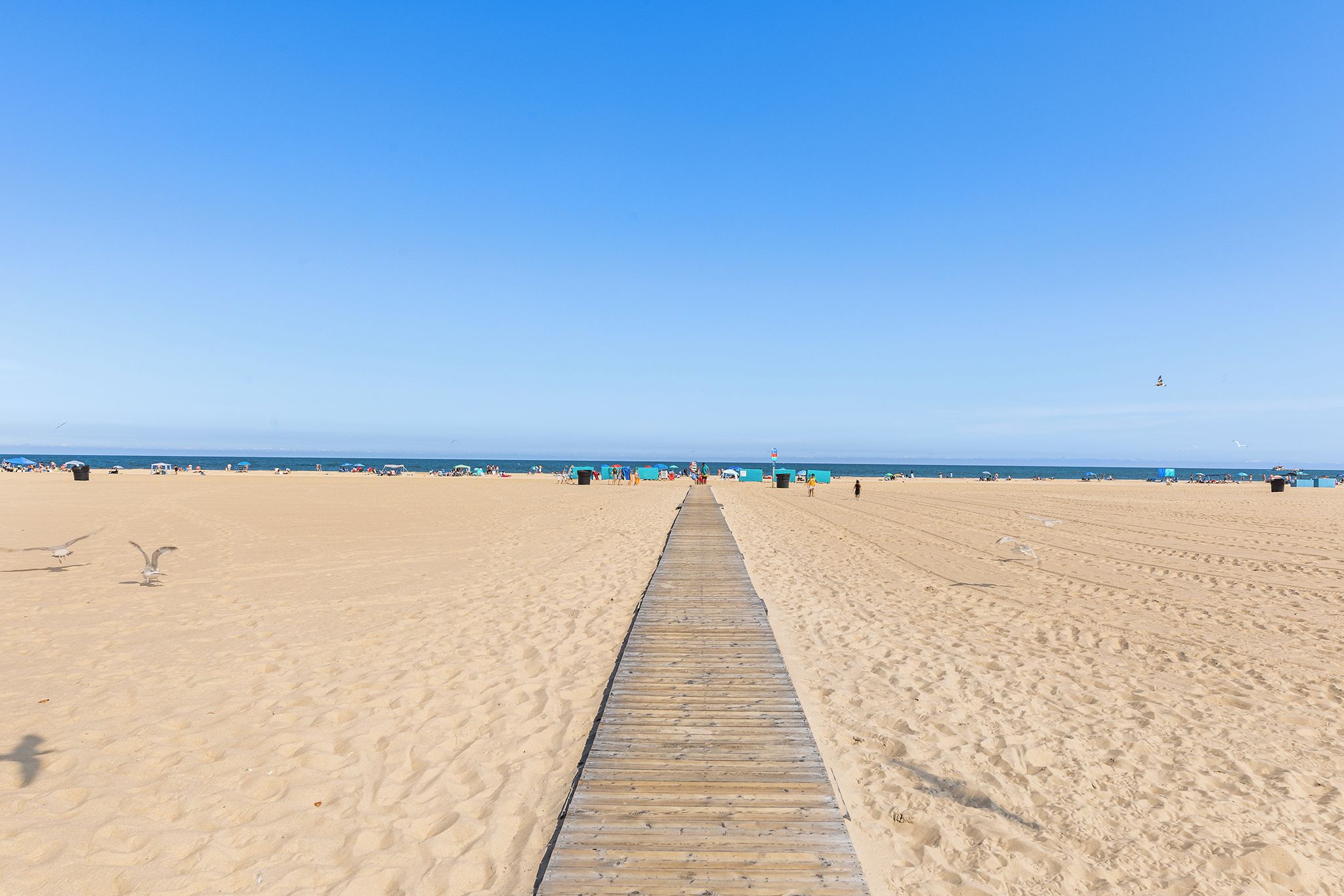 A beach with a wooden walkway leading to the sea, sandy beach, and clear blue sky.
