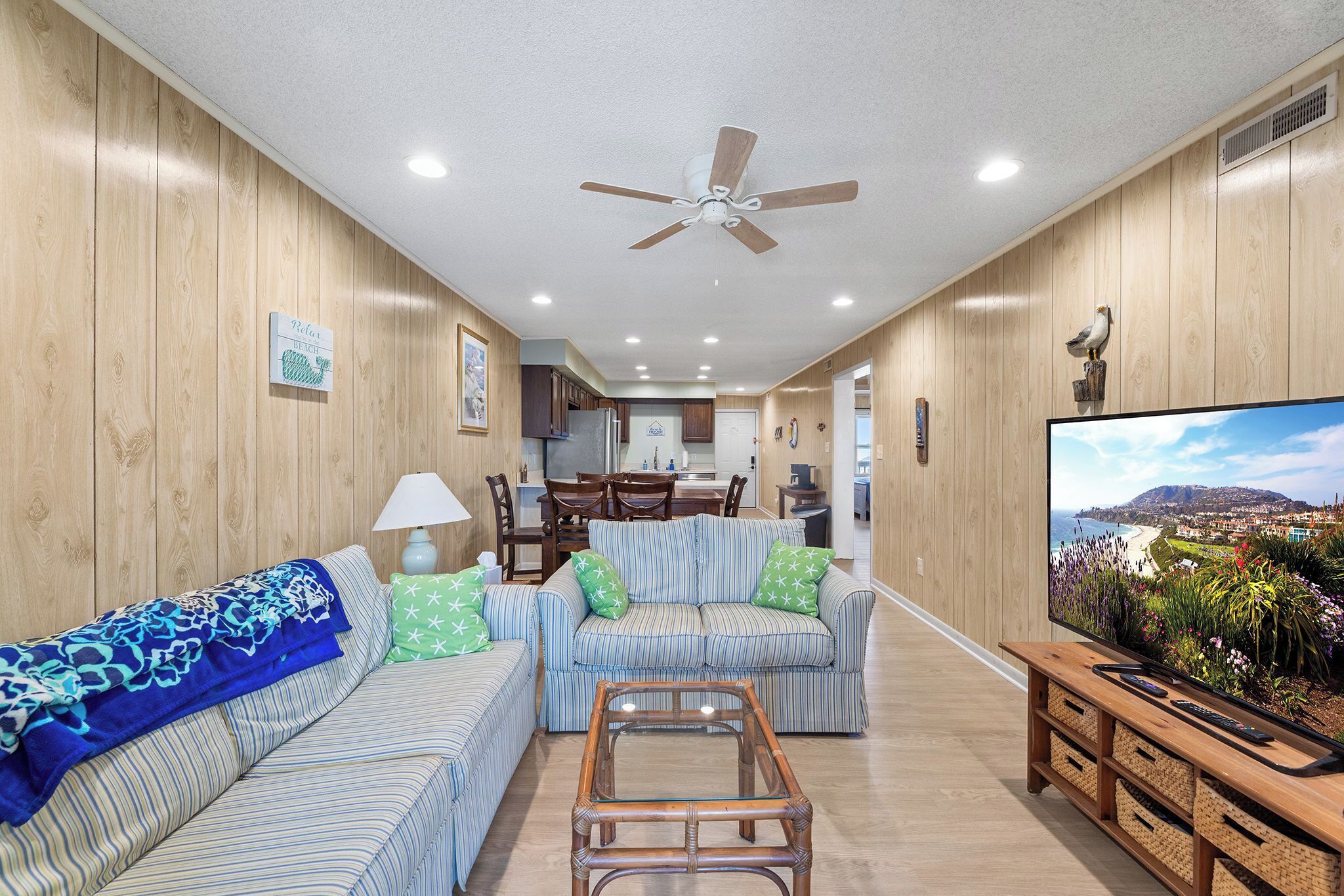 A living room with striped sofas, a glass coffee table, and a television displaying a scenic view.