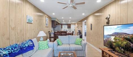 A living room with striped sofas, a glass coffee table, and a television displaying a scenic view.