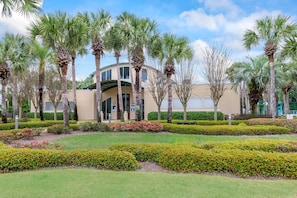 A building with a curved facade, surrounded by well-maintained palm trees and manicured hedges.