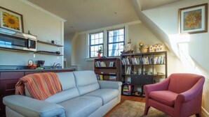 Una sala de estar con un sofá gris, un sillón rojo y una estantería llena de libros.