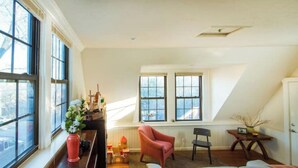 Un acogedor loft con un ventanal grande, un sillón rojo, un sofá gris y una pequeña mesa con una planta.