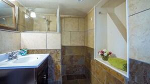 Un baño con lavamanos, espejo, ducha y una pequeña ventana con flores.