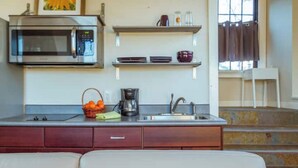 Una cocina compacta con microondas, cafetera y pileta. Hay repisas sobre la mesada con vajilla y una cesta de naranjas.