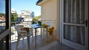 Un balcon avec une table et des chaises, un pot de fleurs et une vue sur les bâtiments en arrière-plan.