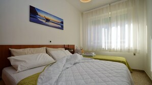 Une chambre d’hôtel avec un lit, une table de chevet, une lampe, un tableau au mur et une fenêtre avec des rideaux légers.