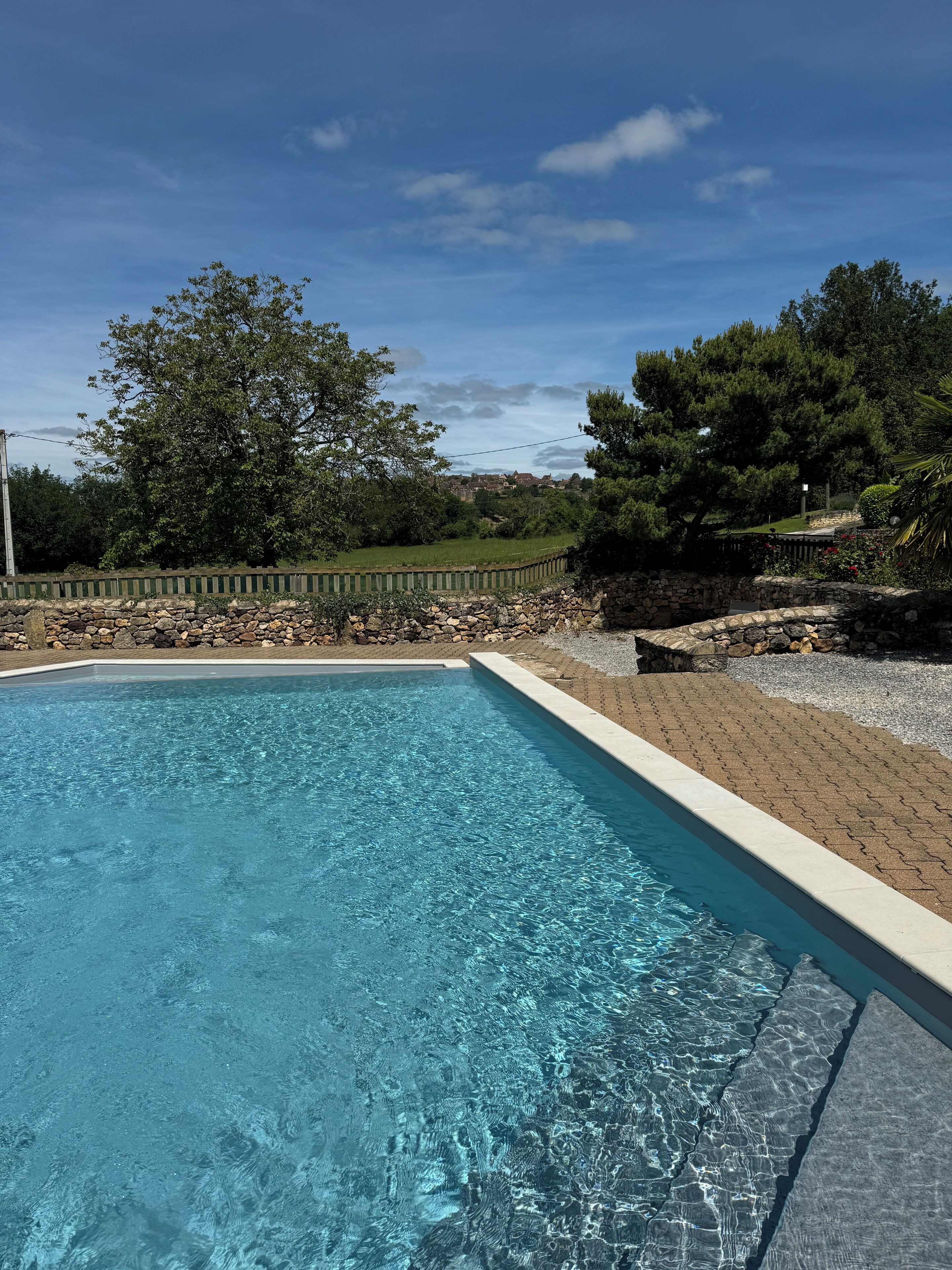 A clear blue swimming pool with a stone wall and a wooden fence in the background.