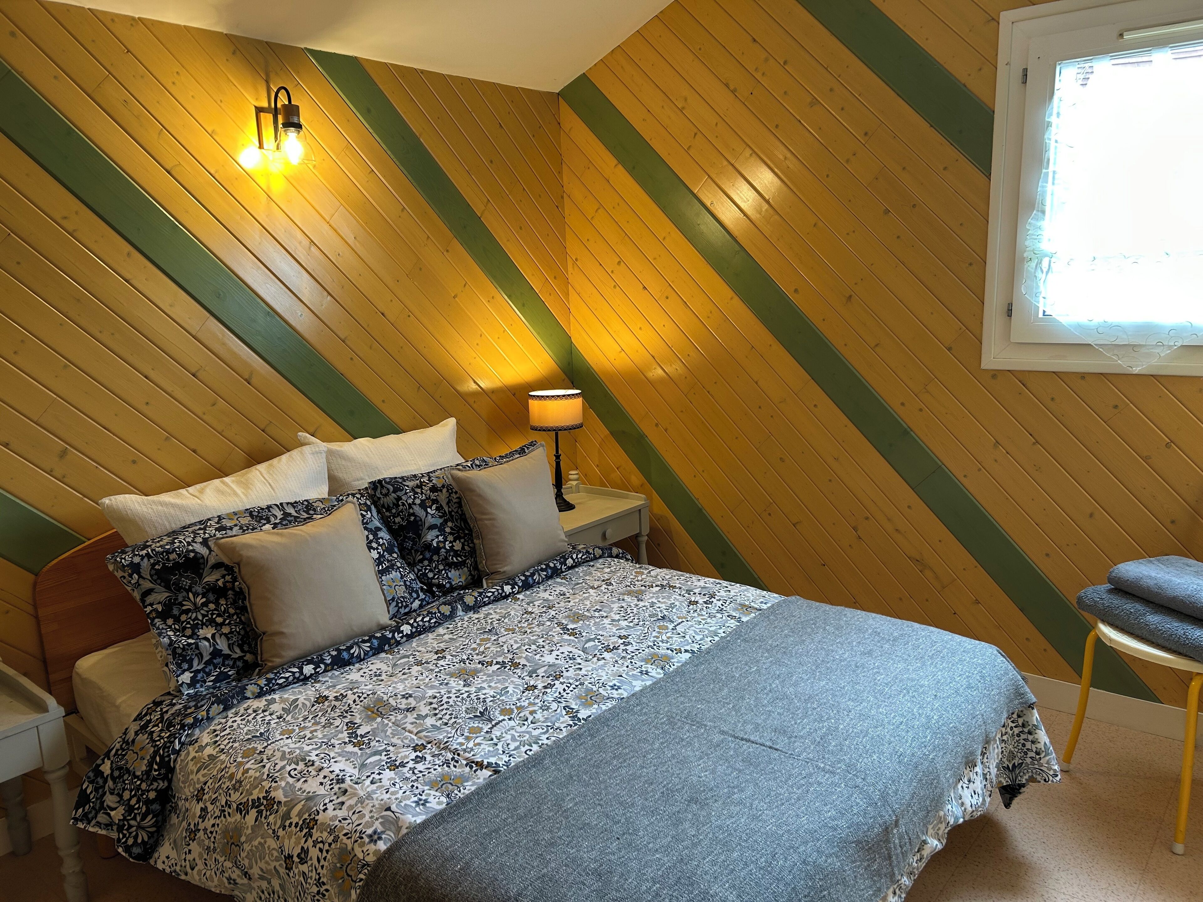 A bedroom with a bed, pillows, a nightstand, a lamp, and a window.