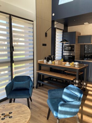 Una cocina moderna con comedor, que incluye una mesa de madera, dos sillas azules y un amplio ventanal con persianas.