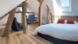 Une chambre avec un plafond en pente, un lit avec une literie blanche et des oreillers rouges, un plancher en bois et un puits de lumière.