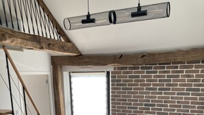 Un salon moderne avec un mur en briques, un escalier en bois et un canapé marron agrémenté de coussins bleus.