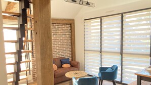 Un salon moderne avec un mur en briques, un escalier en bois et une grande fenêtre équipée de stores.