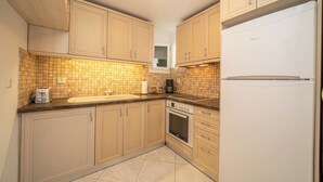 Une cuisine avec des armoires de couleur beige, un réfrigérateur blanc, une cuisinière et un évier.