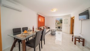 Un coin repas avec une table en verre, des chaises noires et un canapé agrémenté de rideaux orange.