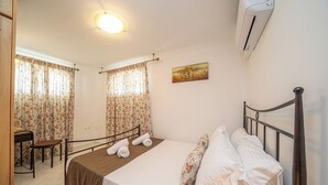 Une chambre d’hôtel avec un lit, un bureau et une chaise. Il y a un tableau au mur et un appareil de climatisation.