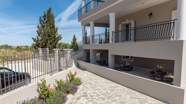 Un immeuble à plusieurs étages doté d’une allée pavée de pierres, de balcons avec des garde-corps en métal et de plantes en pot.