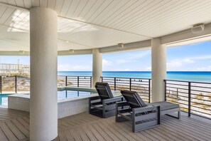 Uma área externa coberta com piscina, espreguiçadeiras e vista para a praia.
