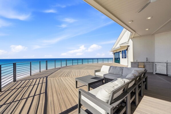 A deck with a sofa, a table, and a view of the ocean.