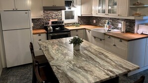 Una cocina con armarios blancos, encimera de mármol, horno empotrado y fregadero.