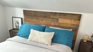 Una cama con cabecera de madera, edredón blanco y almohadas azules y blancas.