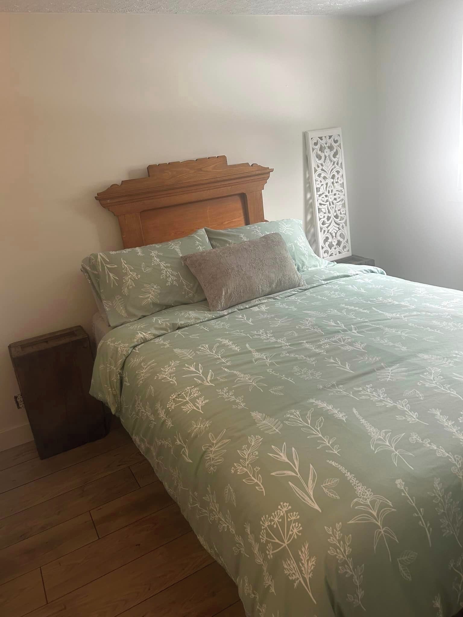 Une chambre à coucher avec une tête de lit en bois, une couvre-lit à motifs floraux verts et une petite commode en bois.