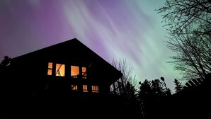 Una casa con silueta oscura contra un cielo nocturno con auroras boreales.