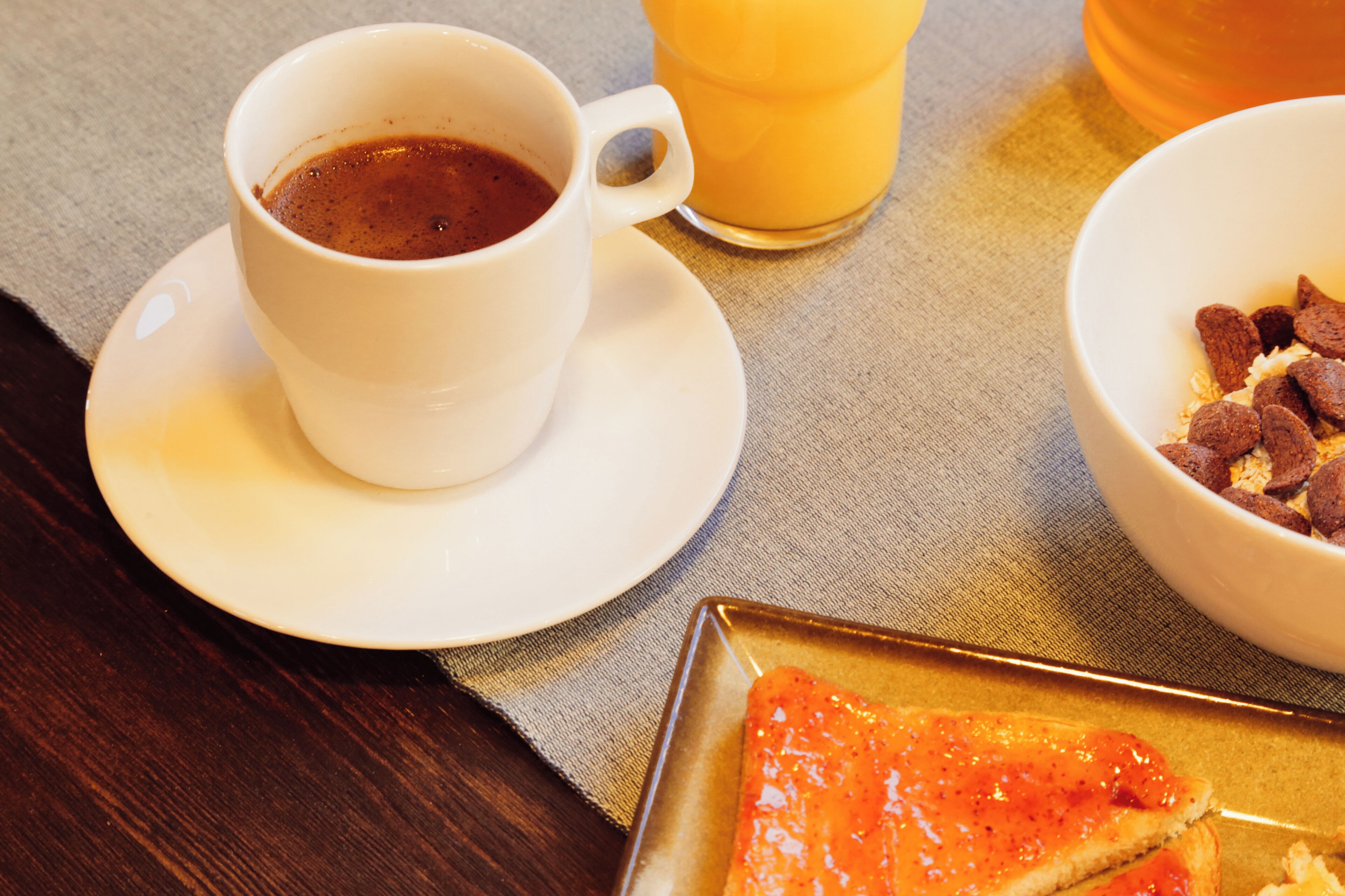 Una escena de desayuno con una taza de café, un vaso de jugo de naranja y un tazón de cereal sobre una mesa.