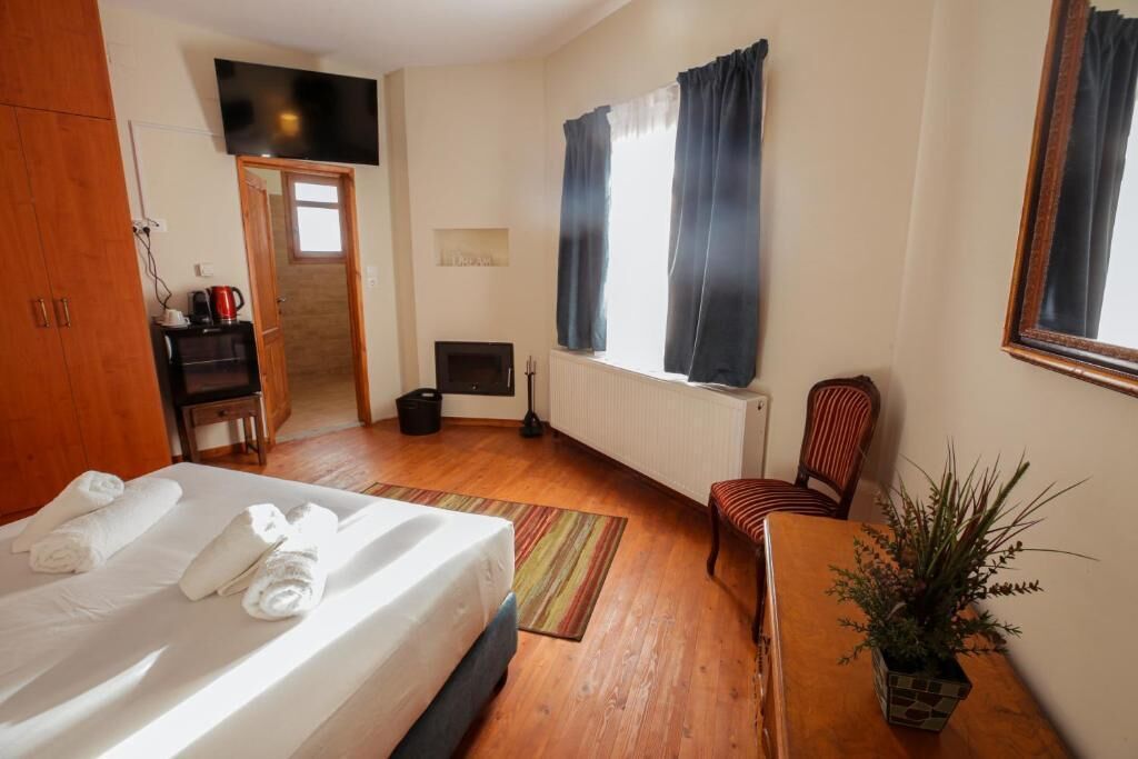 A hotel room with a bed, a desk, a chair, a radiator, and a window with curtains.
