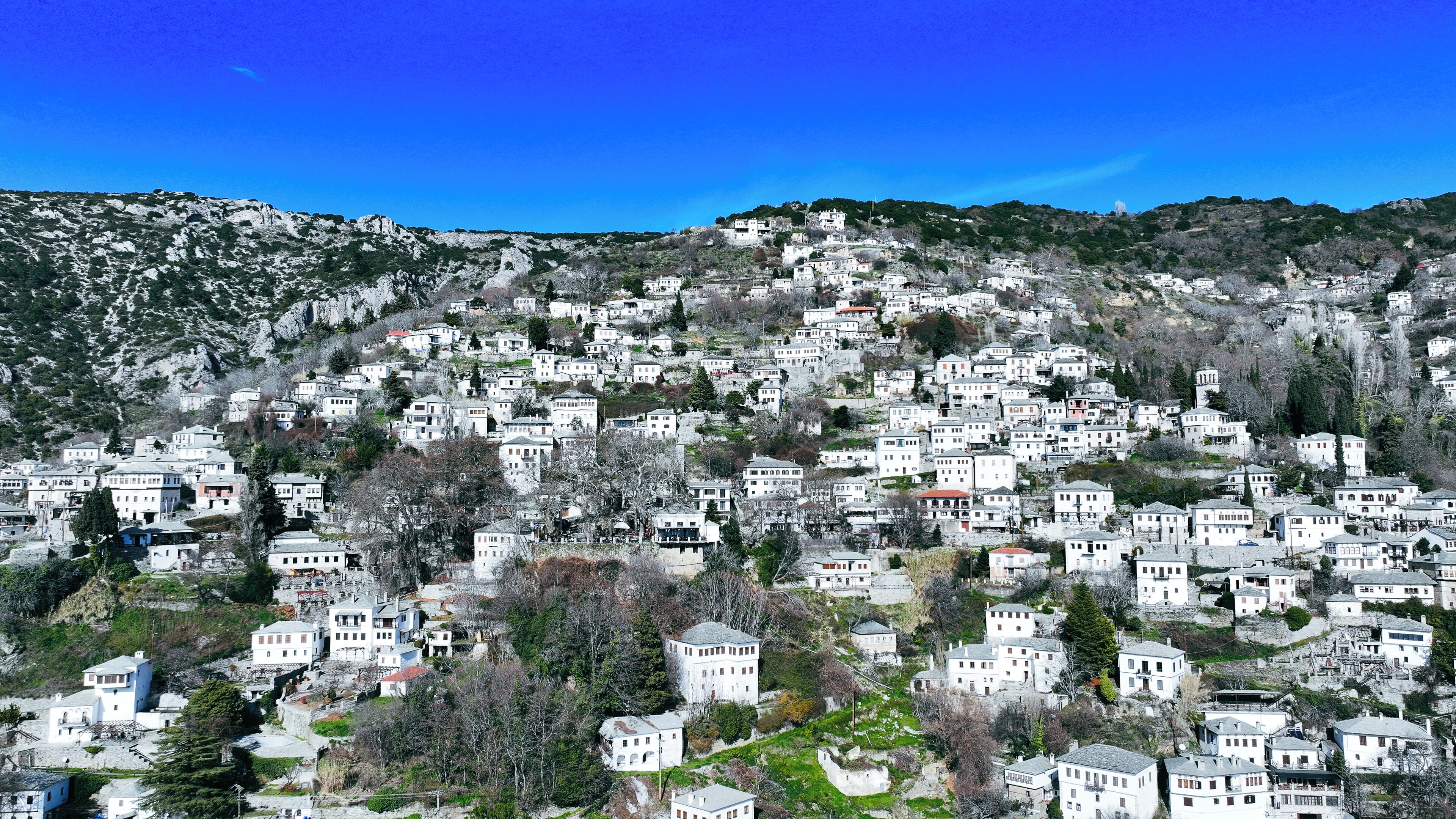A hillside settlement with compact, white buildings, some with red roofs, surrounded by sparse vegetation and rocky terrain.