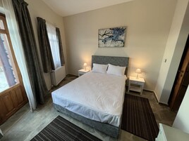 Habitación de hotel con una cama grande, dos mesitas de noche con lámparas, una ventana con cortinas, un radiador y un cuadro en la pared.