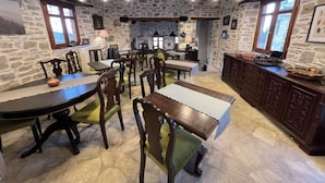 A rustic dining area with stone walls, wooden furniture, and pendant lighting. - AURORA-INN (Volos)