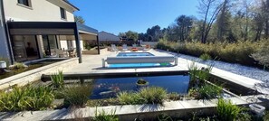A swimming pool with a small pond in the foreground, surrounded by plants and a patio area. - 4CH villa with pergola, swimming pool located 4km from Lac CARCANS and 9km from the Ocean (Carcans)
