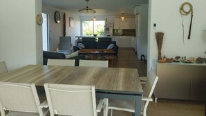 A modern living room with a dining table, sofas, and a kitchen in the background. - 4CH villa with pergola, swimming pool located 4km from Lac CARCANS and 9km from the Ocean (Carcans)