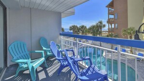A balcony with blue chairs and a pool, overlooking a beach and a building. - Forest Dunes 207 -1BR -Pools, Hot Tub, Lazy River (Myrtle Beach)