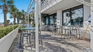 An outdoor patio with tables and chairs, a white railing, and palm trees in the background. - Forest Dunes 207 -1BR -Pools, Hot Tub, Lazy River (Myrtle Beach)