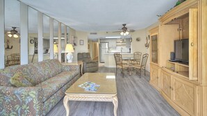 A living room with a sofa, coffee table, and a TV on a wooden cabinet. There is a dining area with chairs and a table. - Forest Dunes 207 -1BR -Pools, Hot Tub, Lazy River (Myrtle Beach)